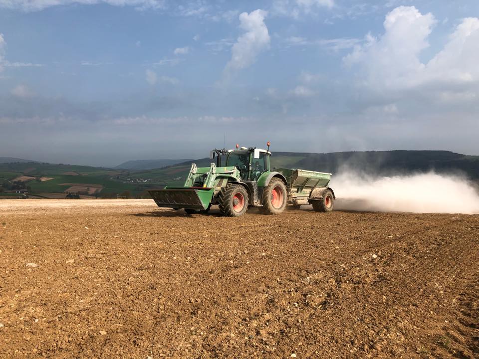 a green and white tractor is plowing a field