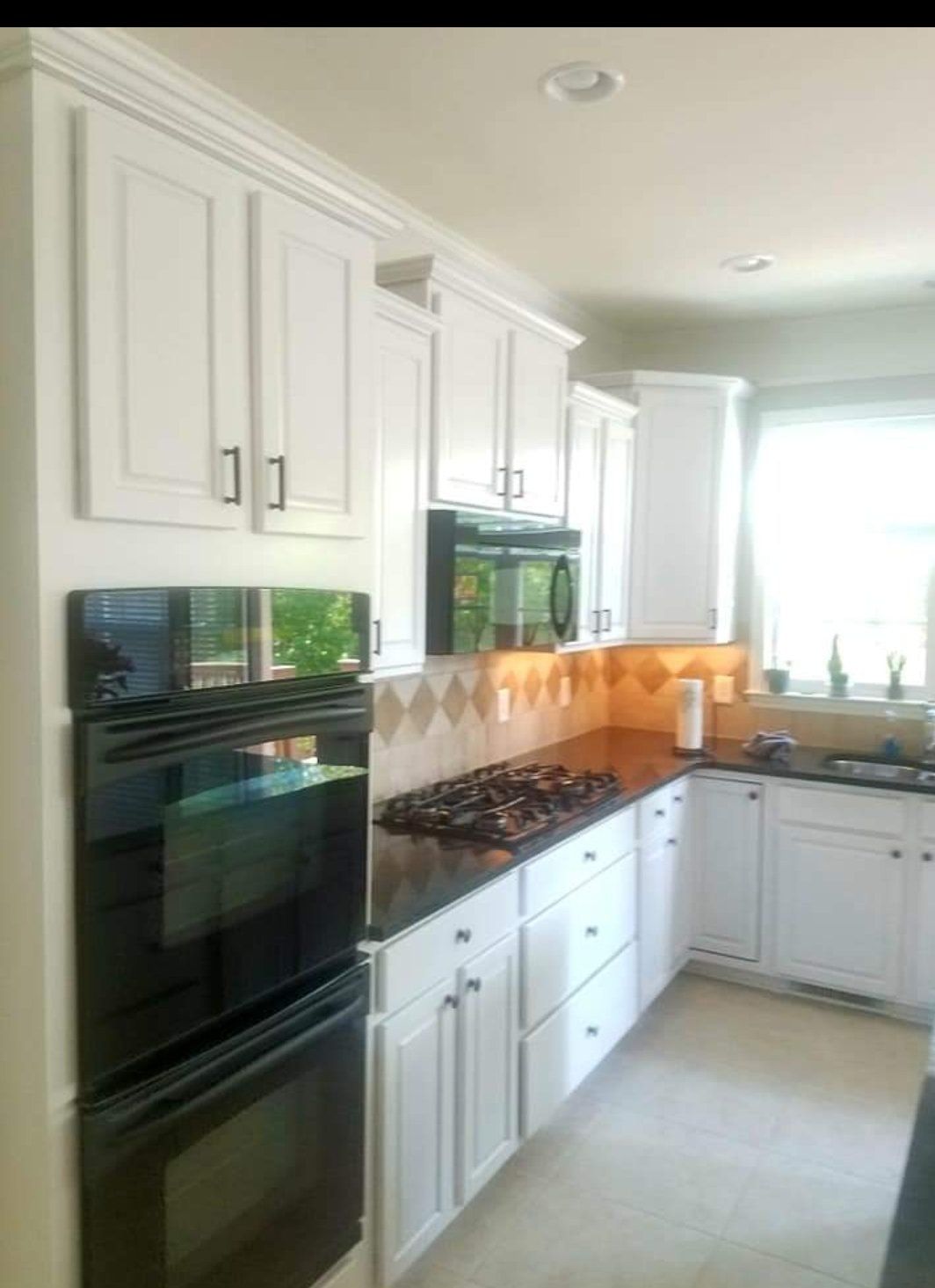 Modern white kitchen with black countertops, a wall-mounted double oven, and a gas cooktop.