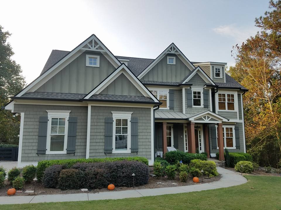 Two-story craftsman-style house with green board-and-batten and shingle siding, a front porch, and fall-decorated landscaping.