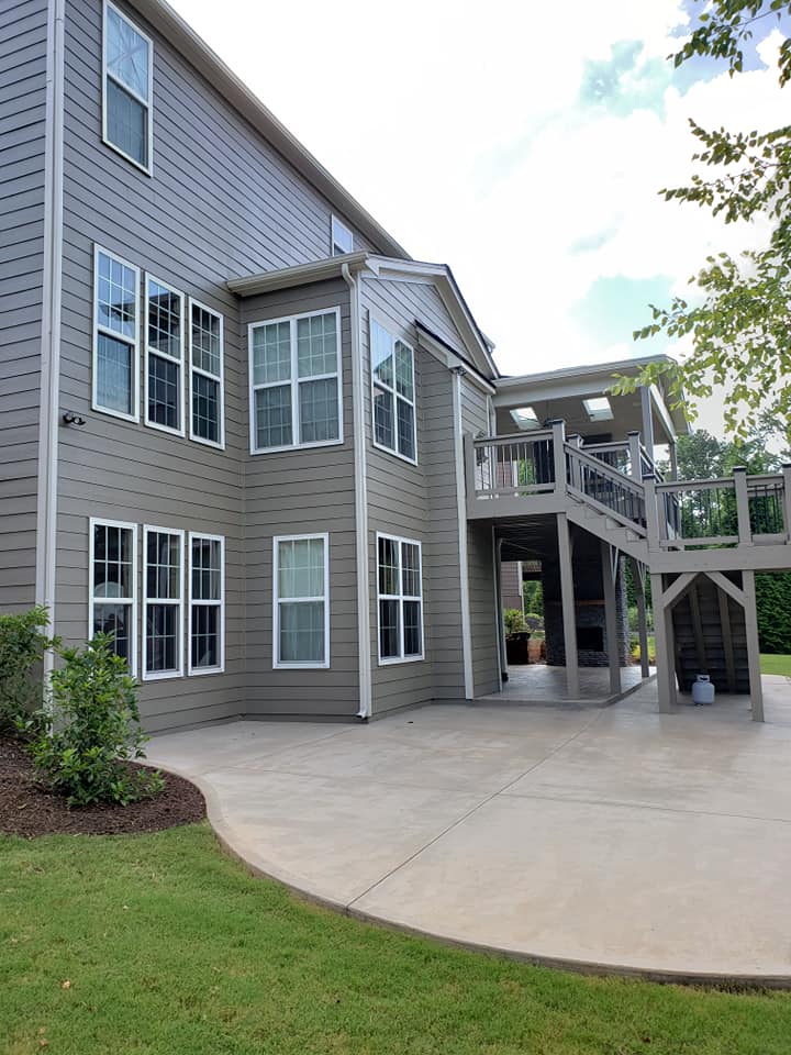 A gray two-story house with a wooden deck, a covered patio underneath, and a concrete patio in the backyard.