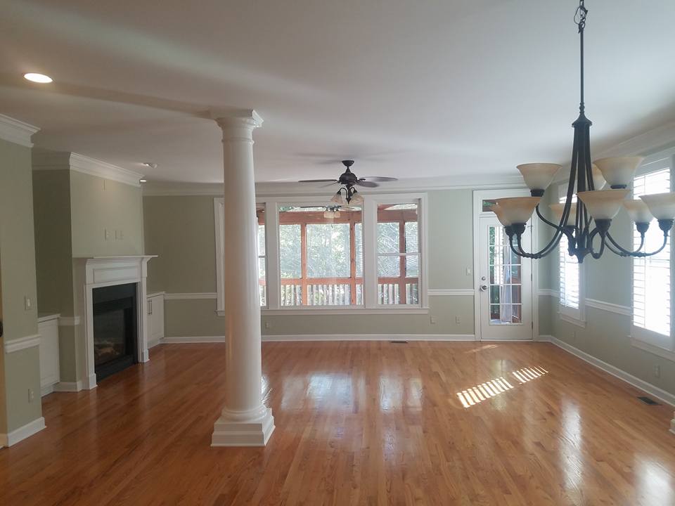 Spacious living room with hardwood floors, a white column, a fireplace, and a large dining chandelier.