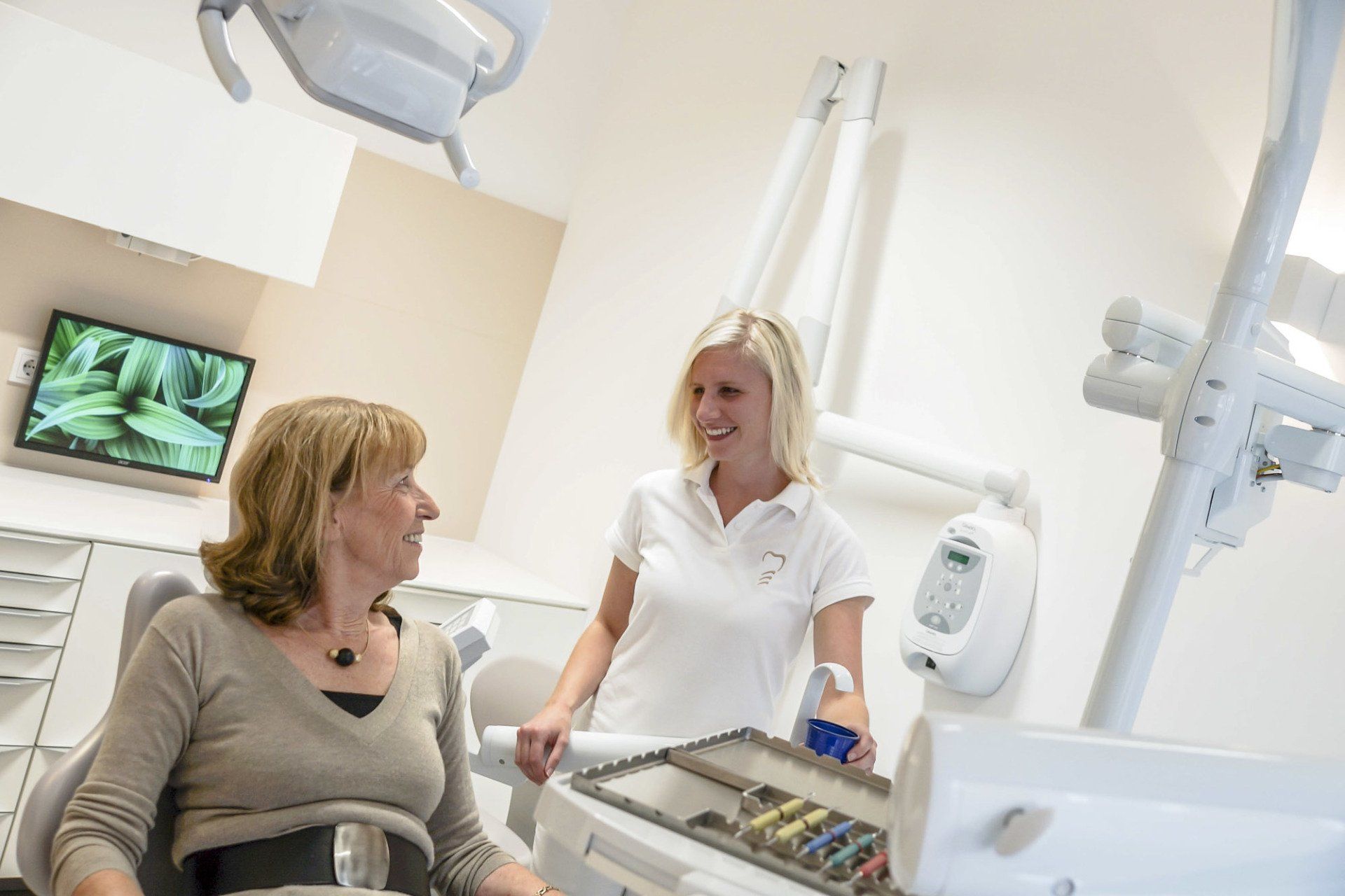 A woman is sitting in a dental chair and talking to a female dentist.