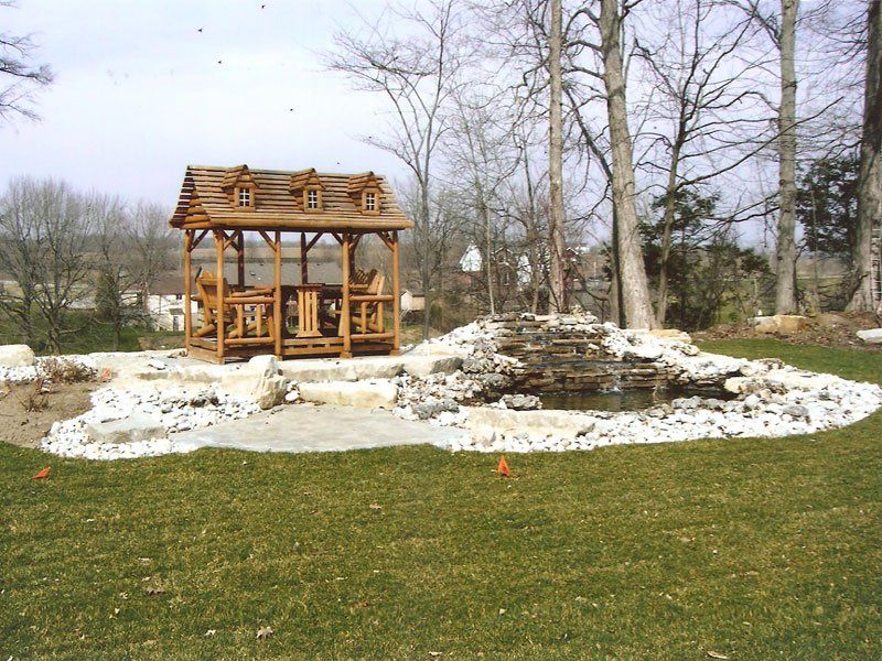 A wooden gazebo sits in the middle of a lush green field