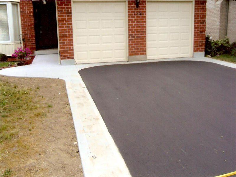 A driveway in front of a brick house with two garage doors
