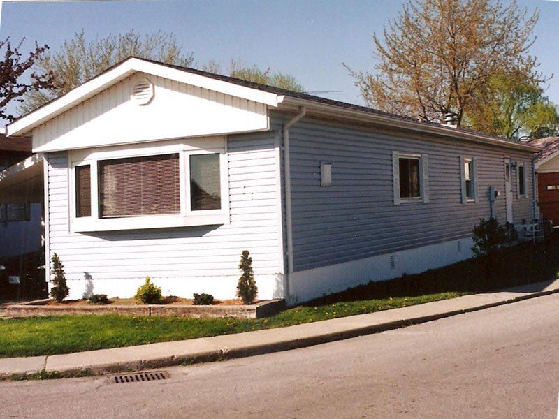 A mobile home with a large bay window sits on the corner of a street