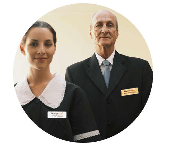Dos empleados del hotel con uniformes negros y placas de identificación, de pie sobre un fondo claro.