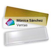Placa identificativa con los nombres “Mónica Sánchez” y “Ventas”, logotipo colorido y soporte de plástico transparente.