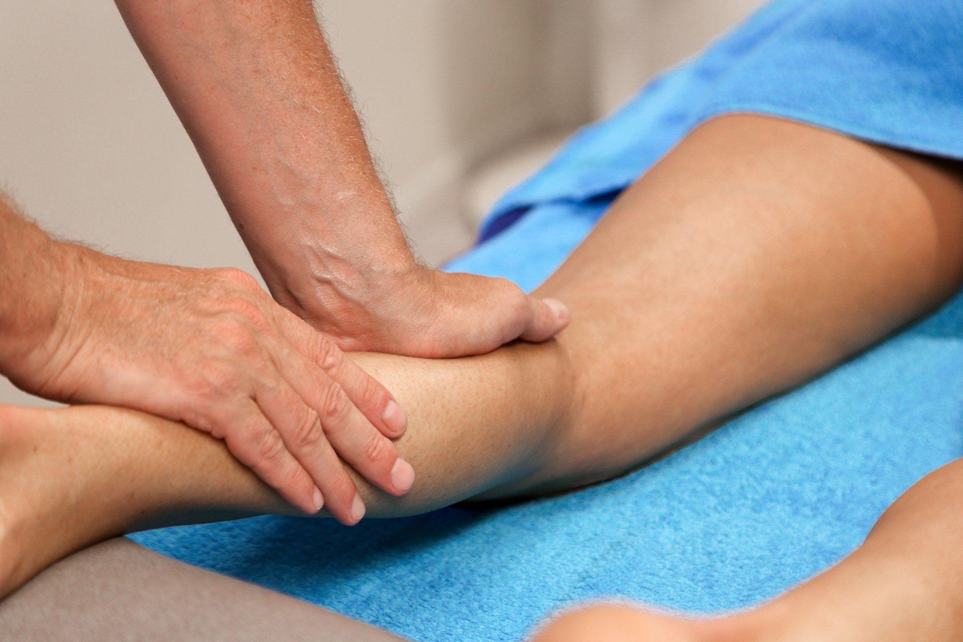Een man geeft een vrouw een beenmassage op een blauwe handdoek.
