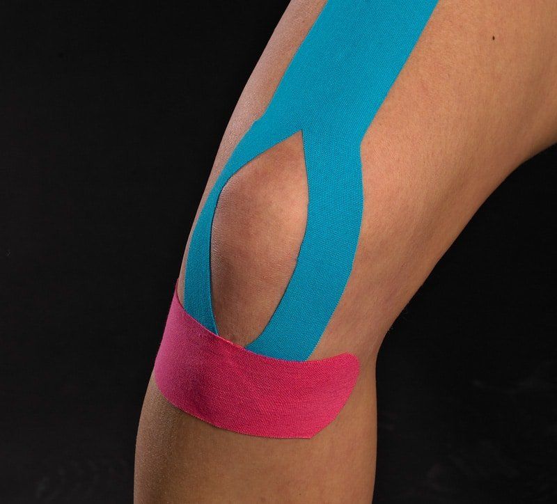 Een close-up van de knie van een persoon met blauwe en roze kinesiotape