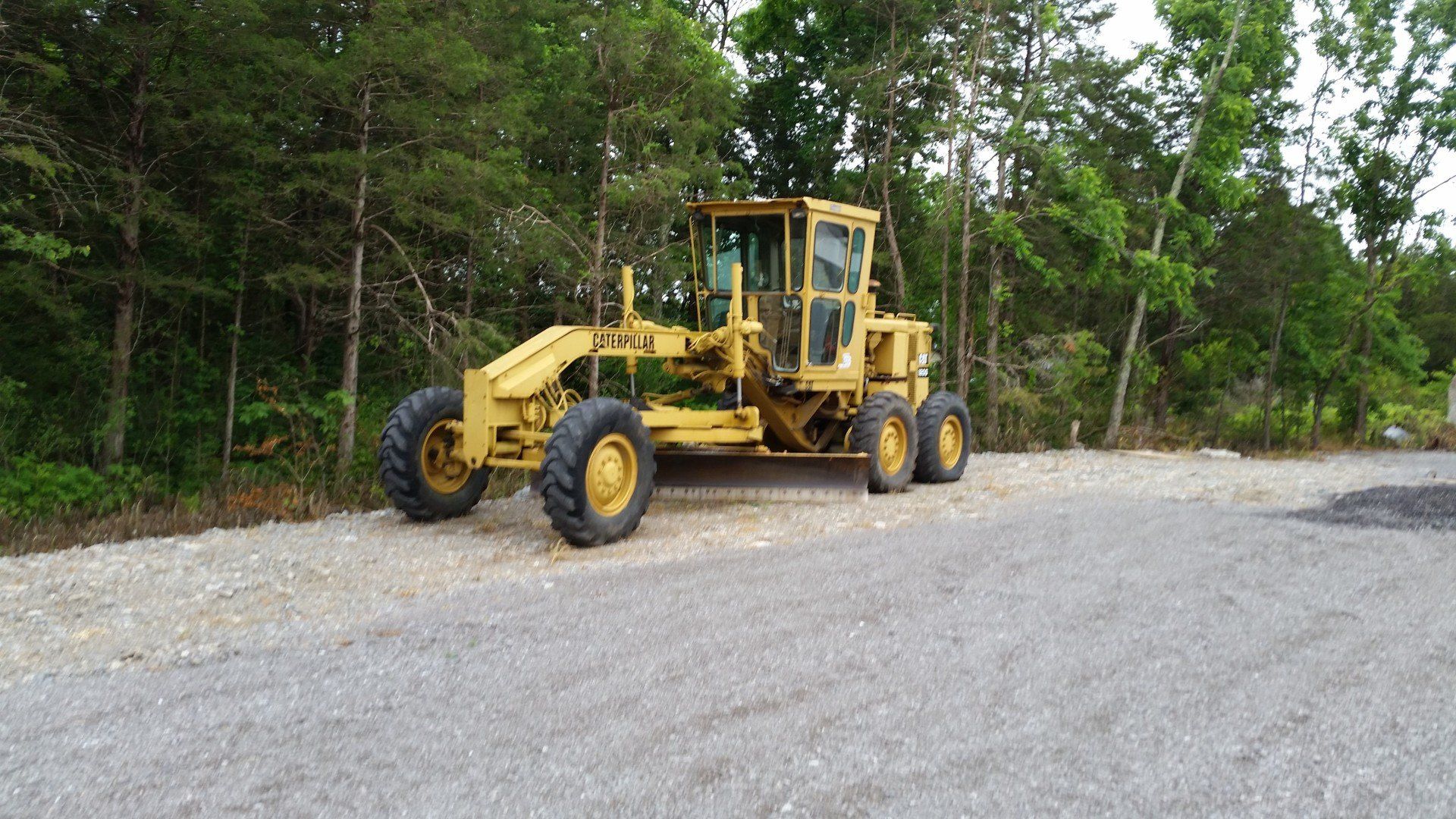 A yellow tractor is parked in a gravel lot.