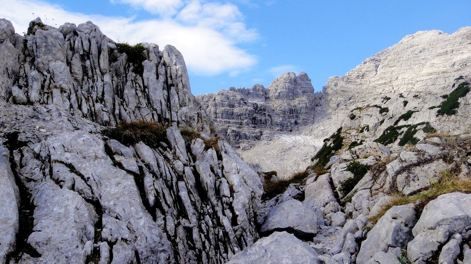 Zerklüftete, weißgraue Bergfelsen unter blauem Himmel mit Wolken.