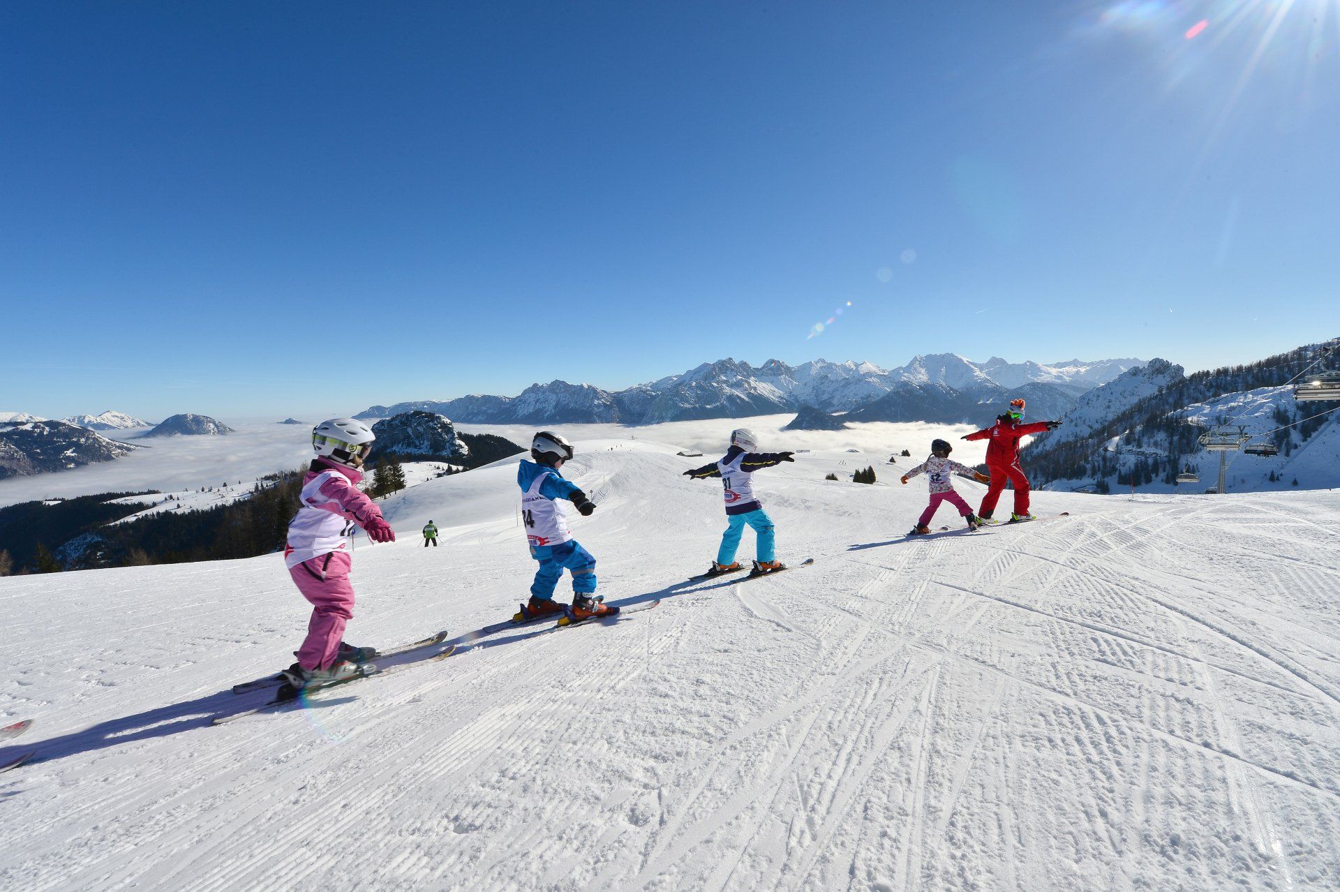 Skifahrer in bunten Jacken, die unter klarem, blauem Himmel einen schneebedeckten Berghang hinabfahren