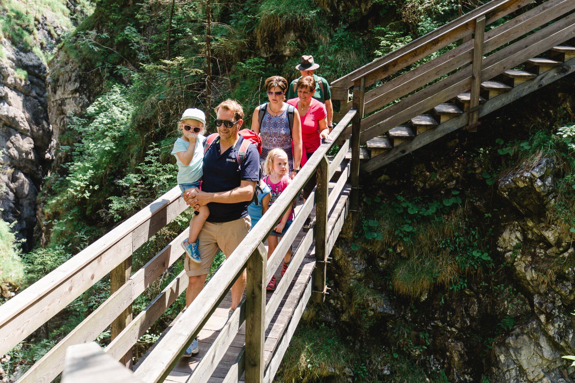 Eine Gruppe wandert über eine hölzerne Treppenbrücke in einer bewaldeten Schlucht hinab.