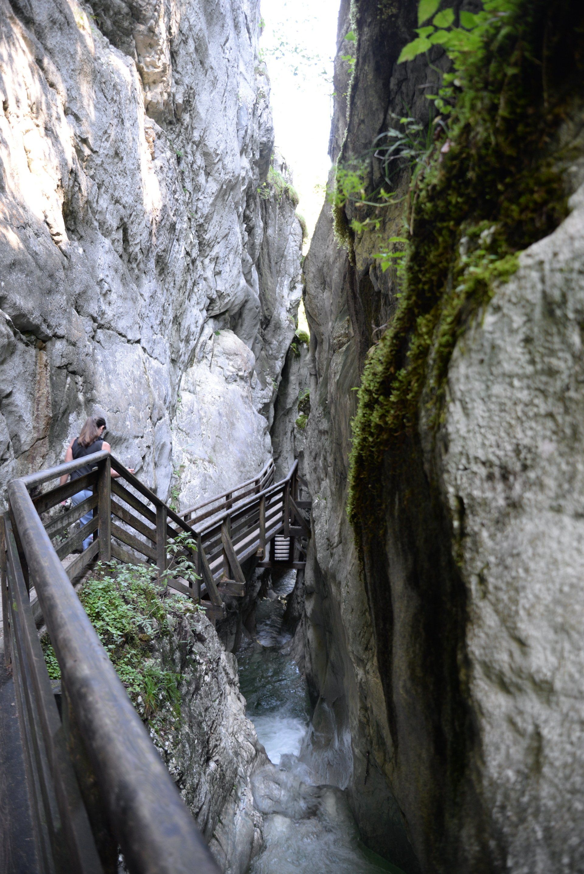 Schmaler Canyonpfad neben einem rauschenden Bach, mit Holzgeländern und moosbewachsenen Felswänden