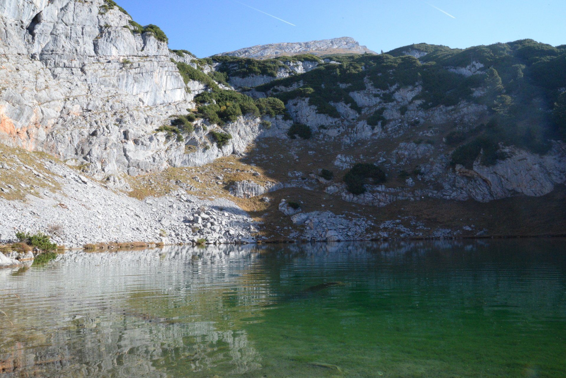 Weiße Felswände über einem grünen Bergsee unter klarem, blauem Himmel