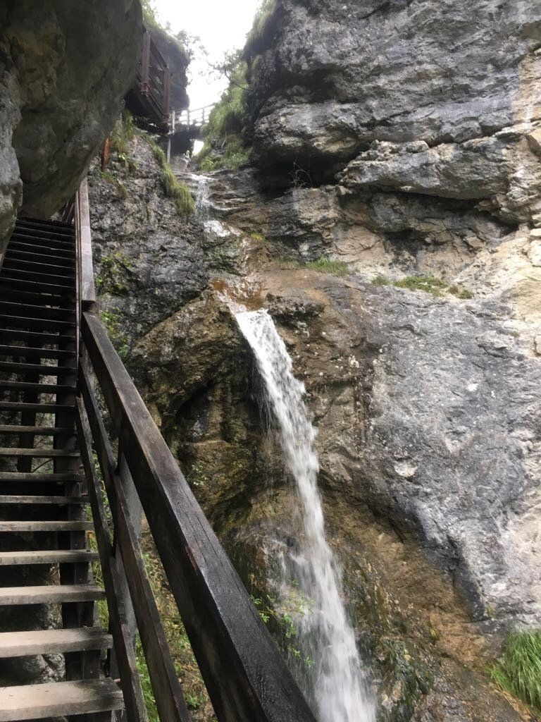 Steile Steintreppe neben einer Felswand und einem kleinen Wasserfall in einer engen Schlucht