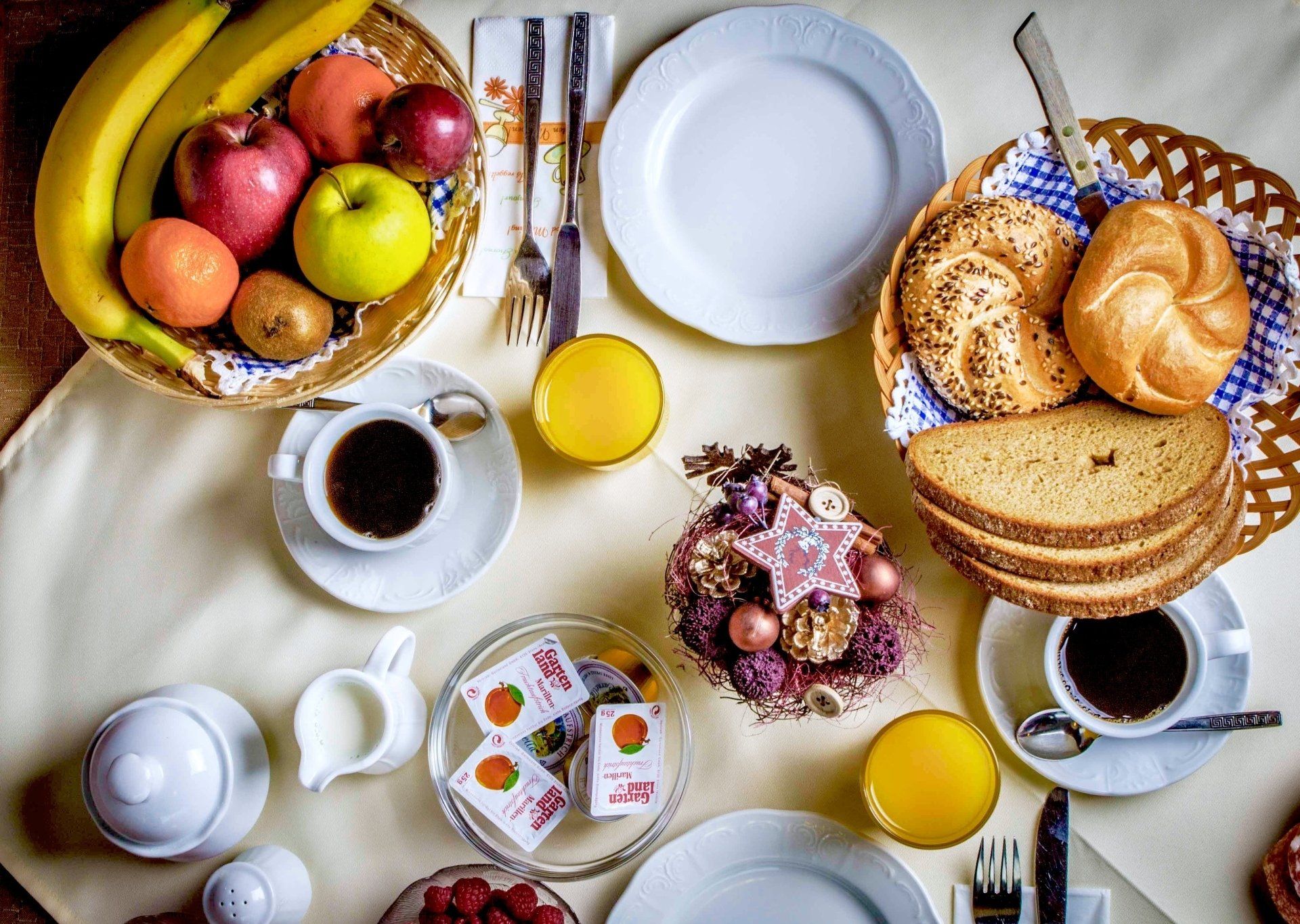 Frühstückstisch mit Obstkorb, Brot, Kaffee und Tellern auf einer weißen Tischdecke