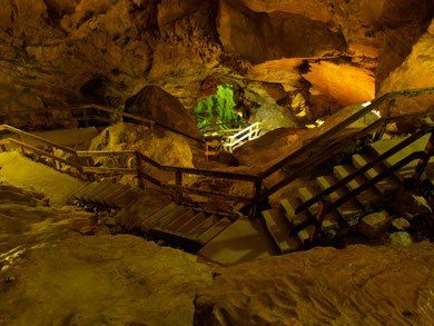 Beleuchtetes Höhleninneres mit Holztreppen und Geländern, die durch felsige Tunnel führen
