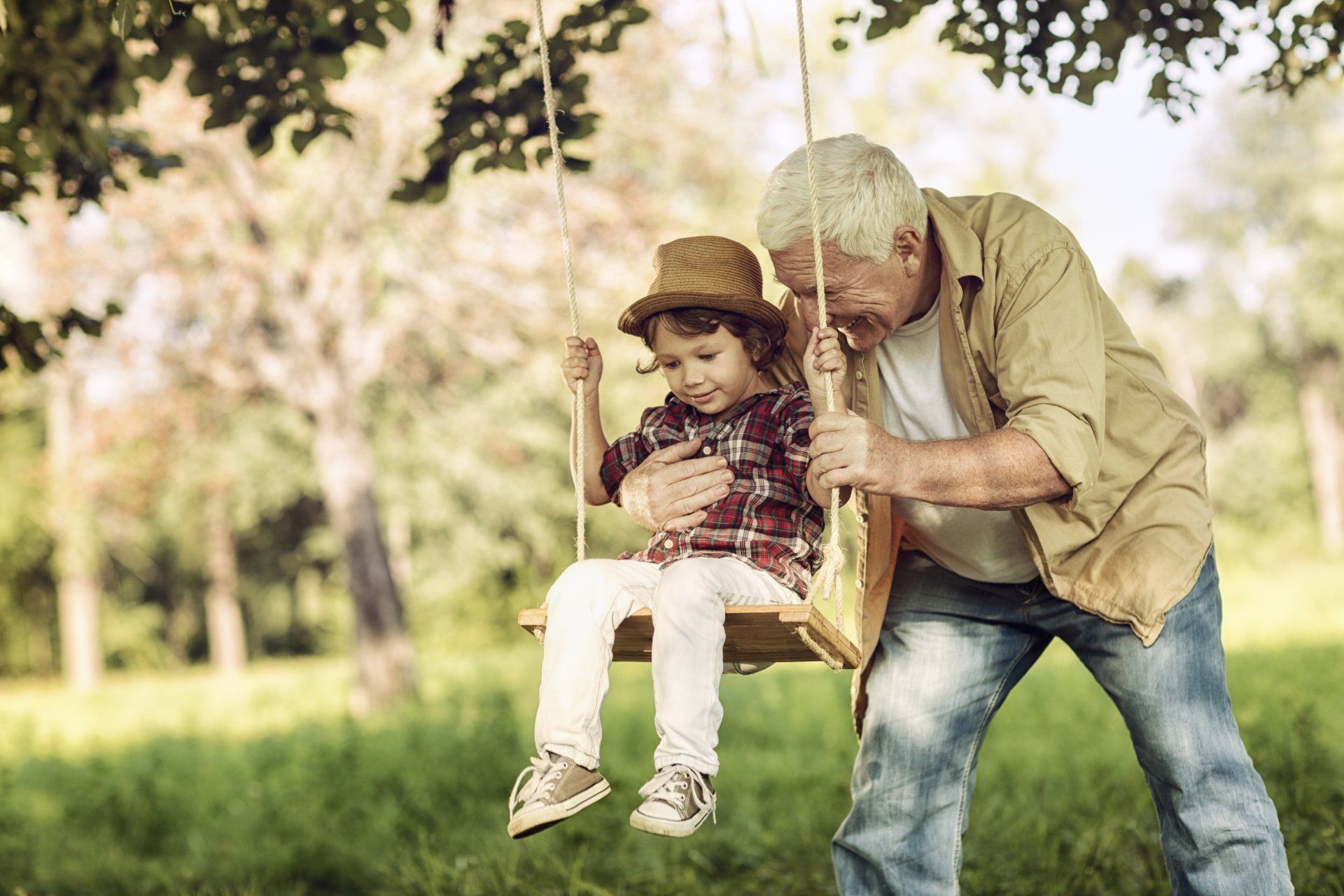 An older man pushing a young boy on a swing.
