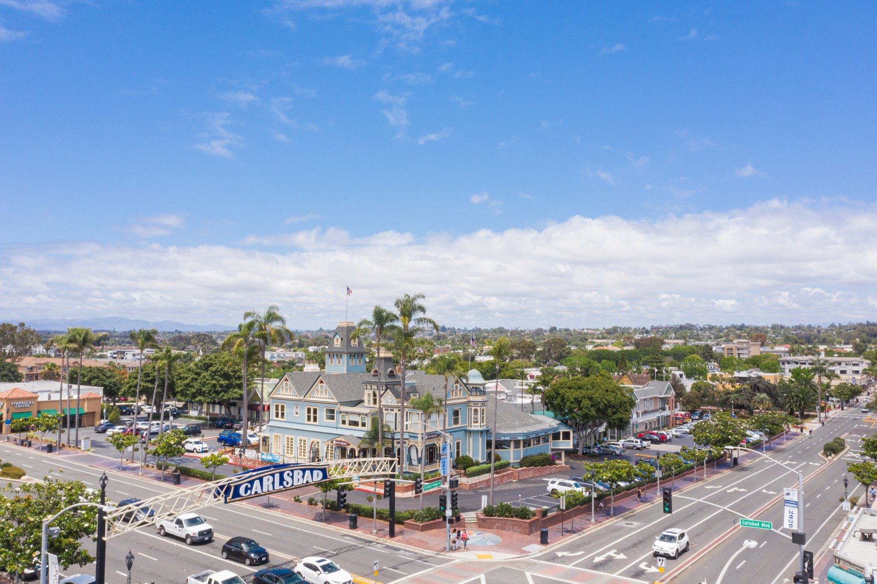 An aerial view of a city street with cars driving down it on a sunny day.