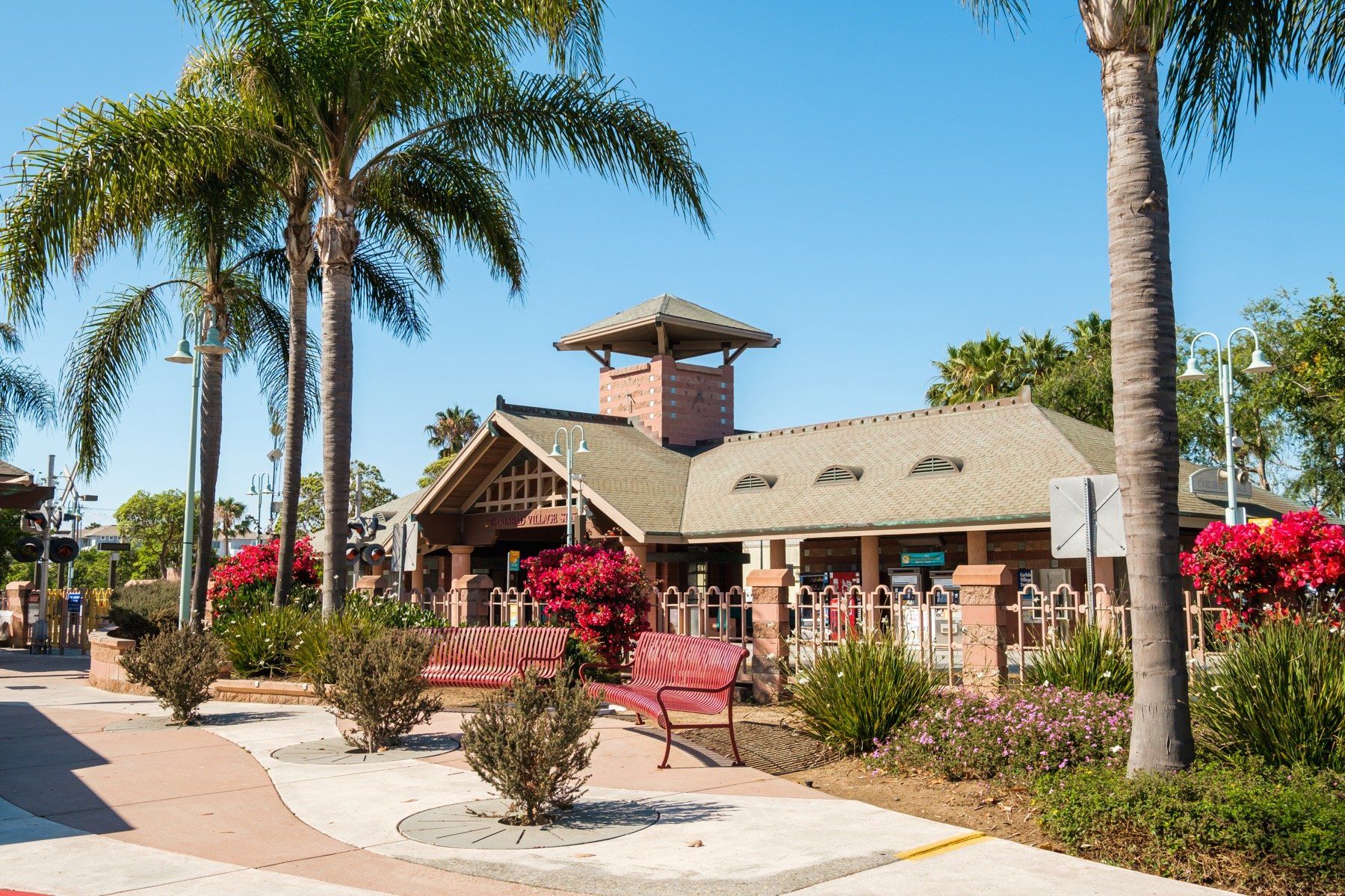 A building with a tower on top of it is surrounded by palm trees and flowers.