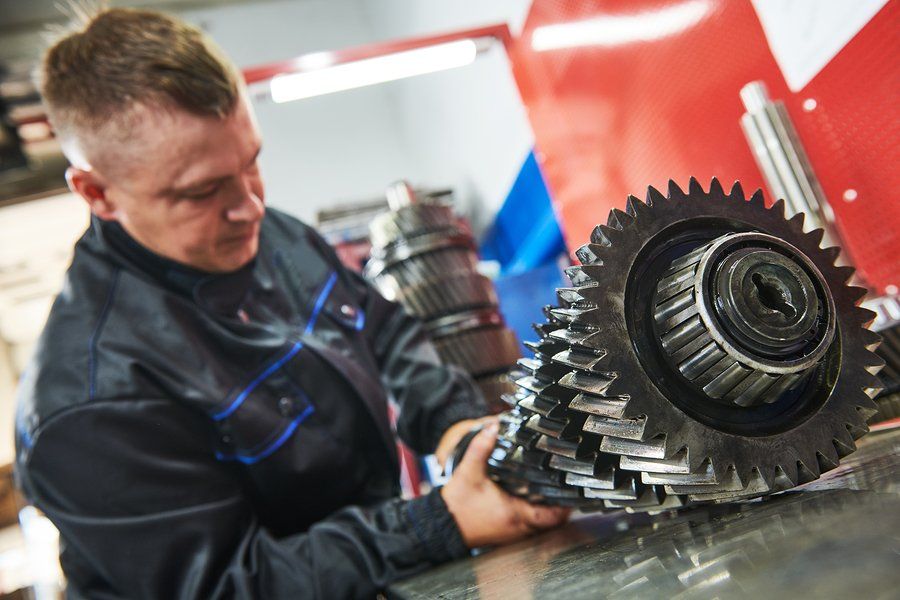Mechanic holding a large gear assembly in a repair shop.