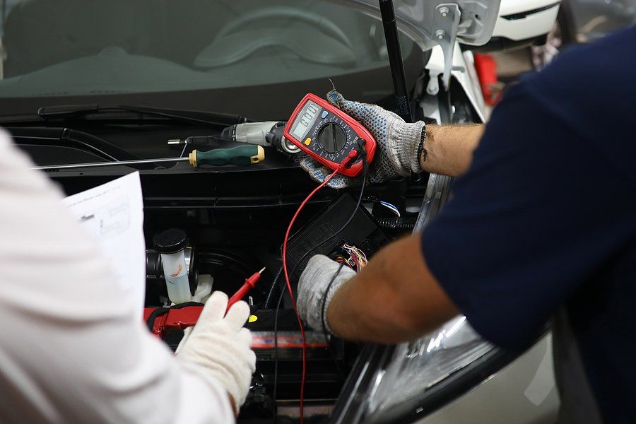 Mechanic uses a multimeter to test a car's battery in a garage.