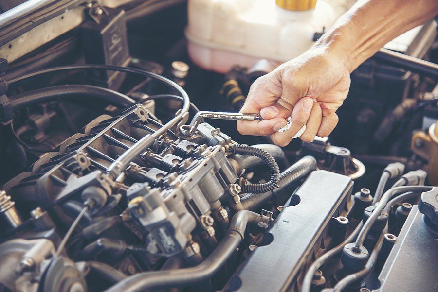 Hand working on car engine, holding a tool, focused on repairs.