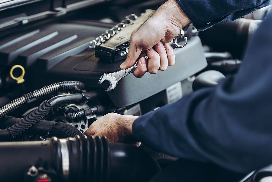 Mechanic working on car engine, using wrench. Tools on the engine cover.