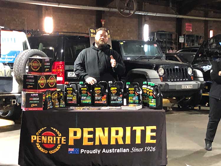 Man at a Penrite oil display giving a thumbs up in a garage with cars.