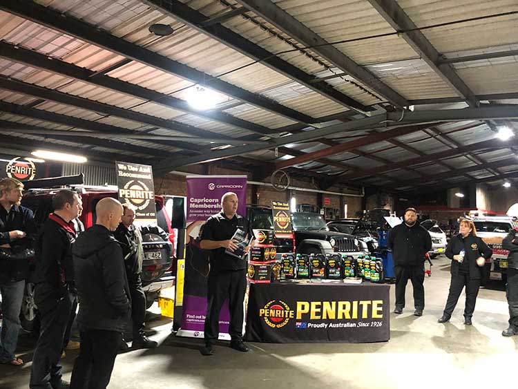 A man presenting Penrite oil products to a group in a warehouse setting.