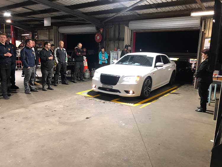 White car in garage with people watching.