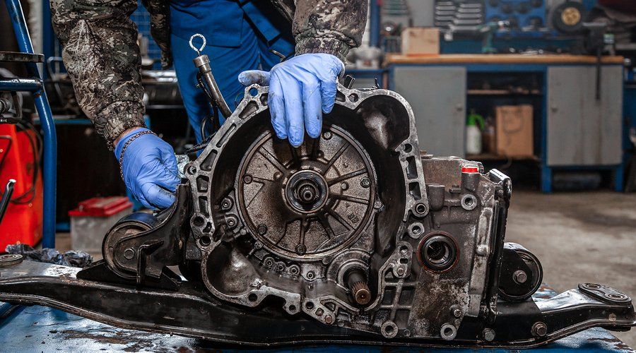 Mechanic in blue gloves working on an open car transmission.