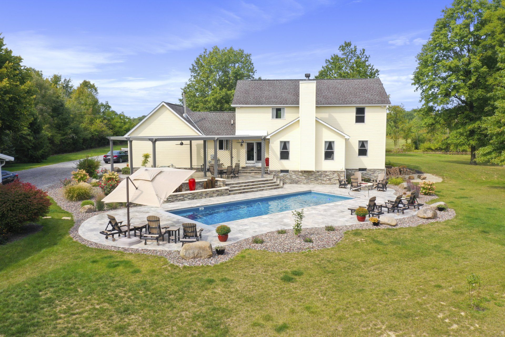 Suburban home with a backyard pool, patio seating, and a large grassy lawn under a blue sky