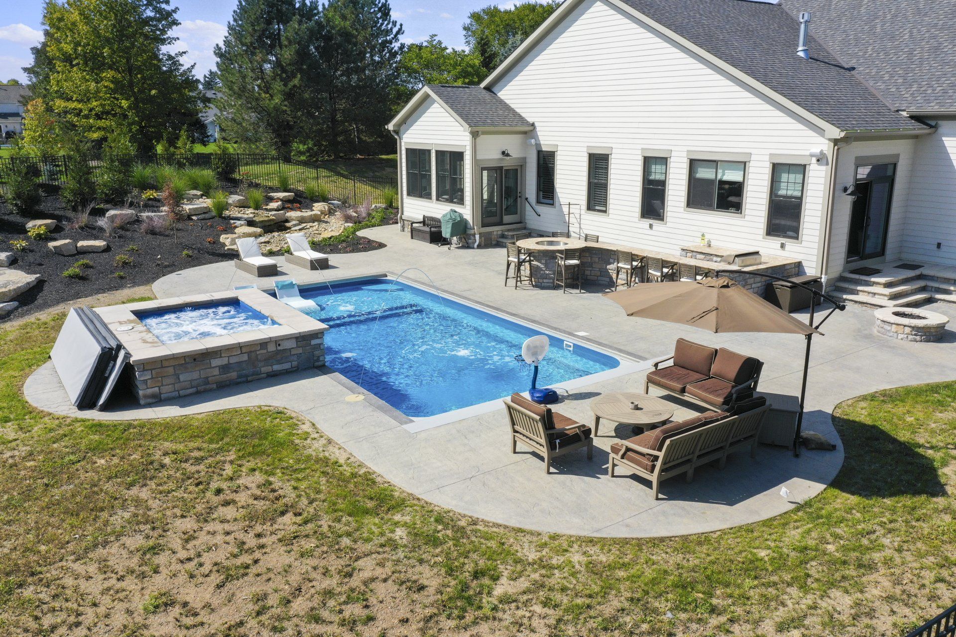 Backyard pool and patio beside a white house with lounge chairs and umbrellas