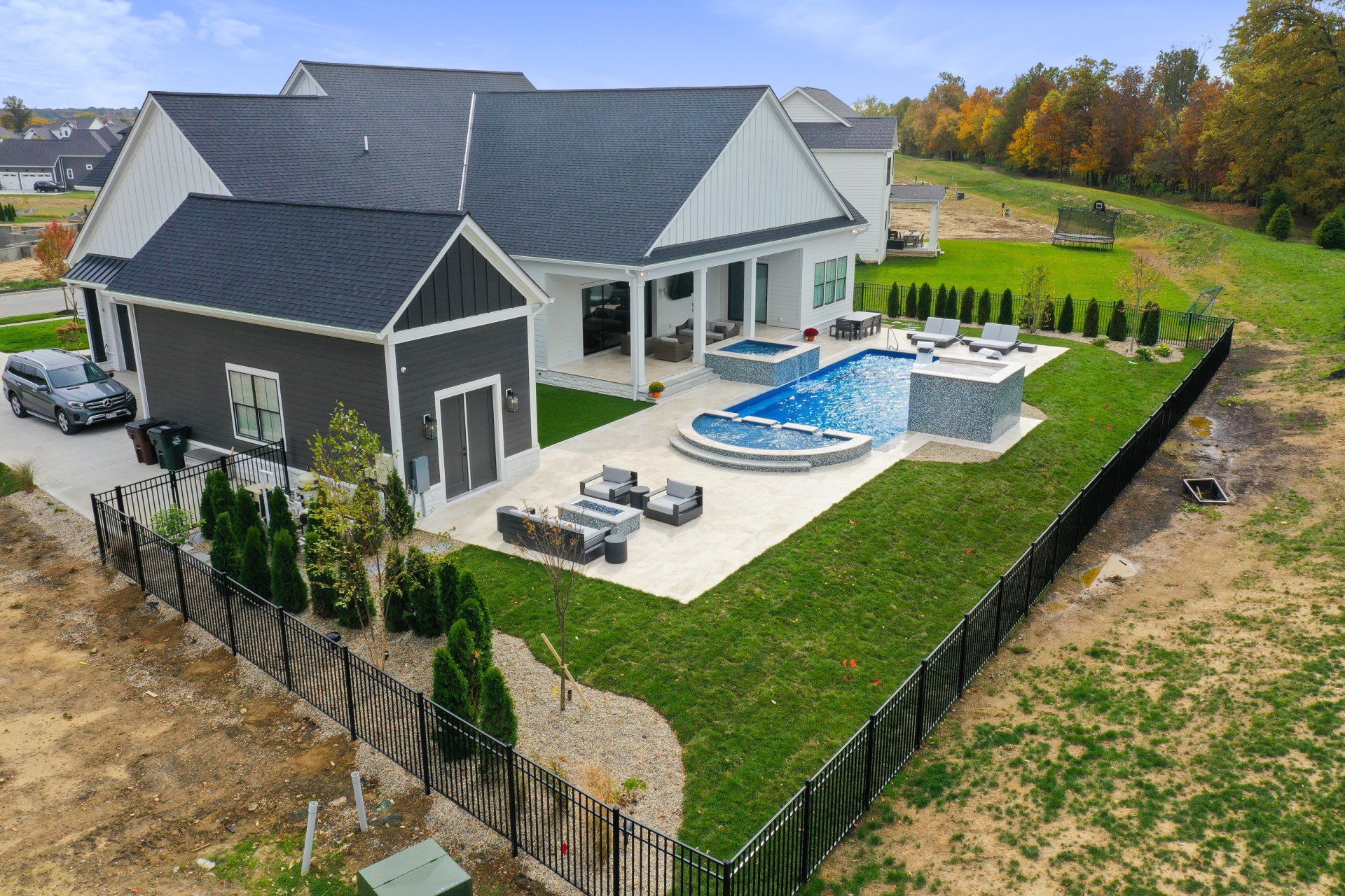 Aerial view of a modern gray house with a fenced backyard, patio, and blue swimming pool