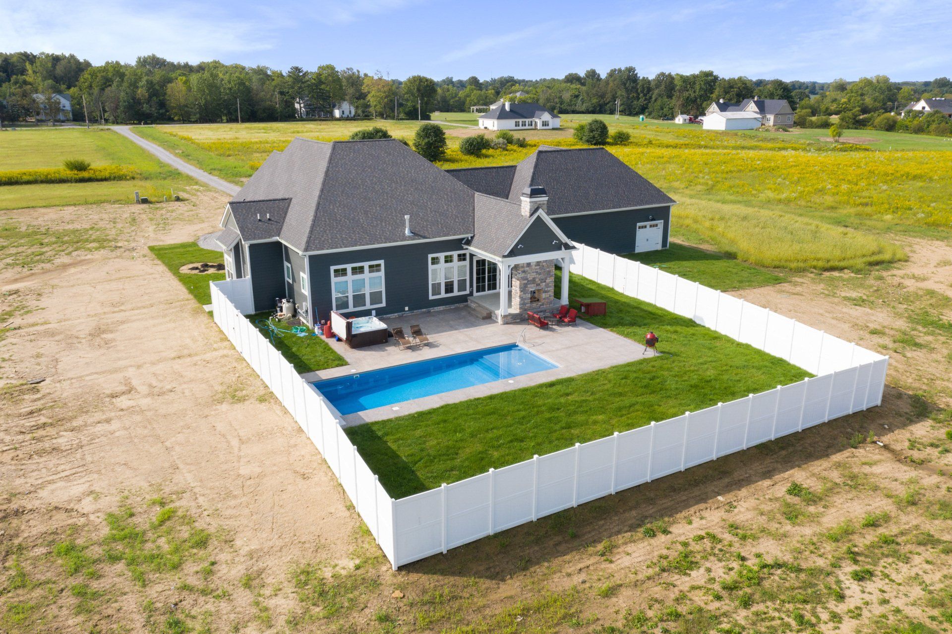 Aerial view of a gray house with a backyard pool and white fence in a rural field.