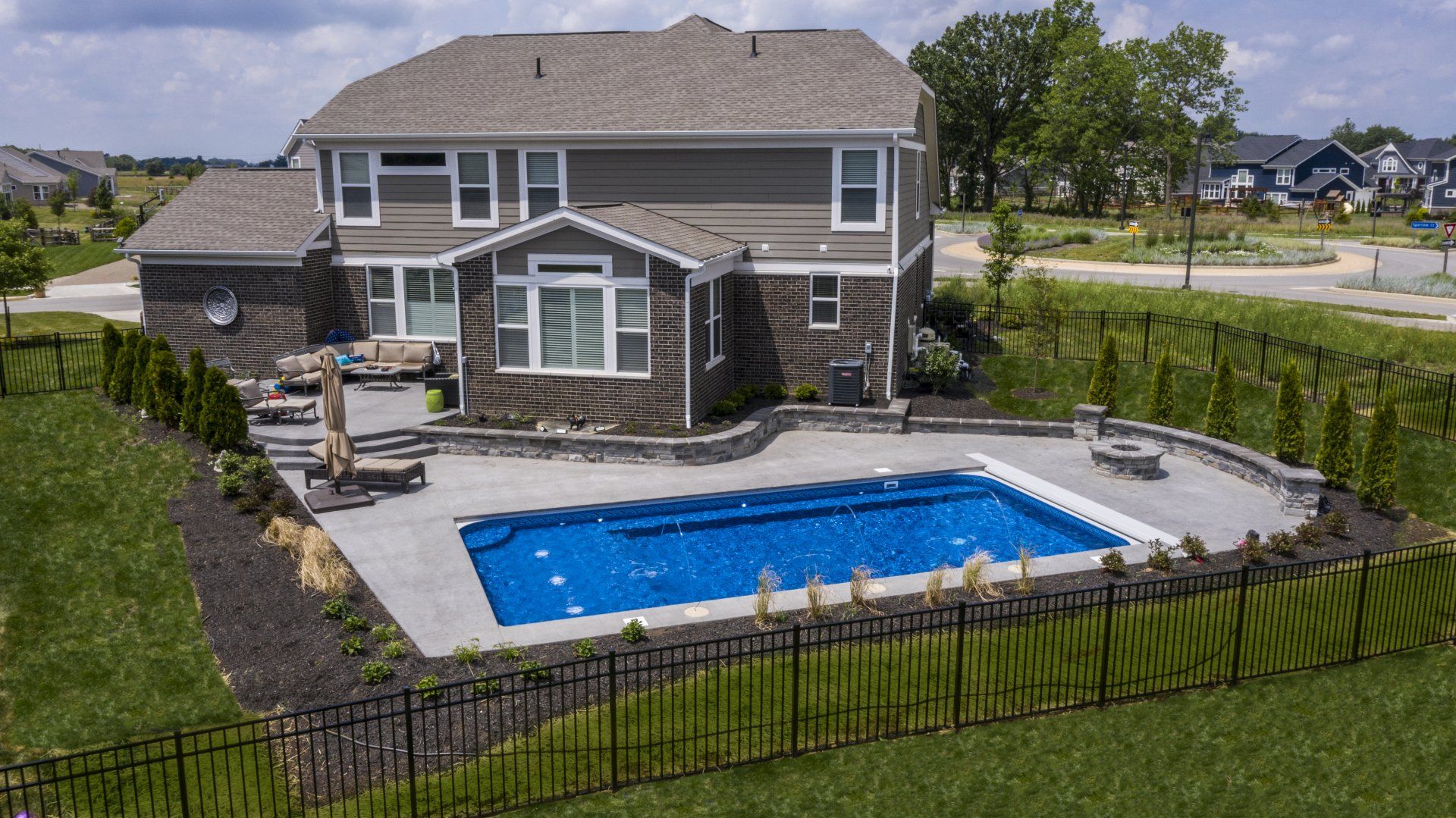 Suburban backyard with a two-story house and a fenced-in blue swimming pool.