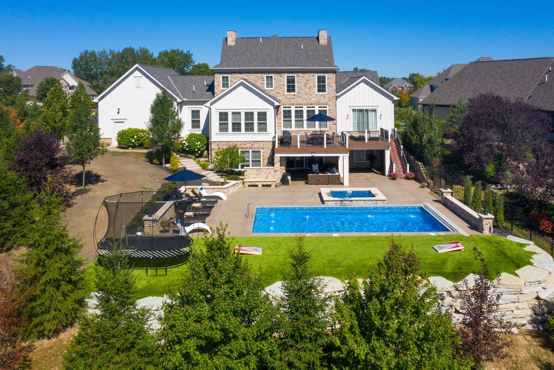 Large suburban house with a backyard pool, patio, and landscaped lawn under a clear blue sky