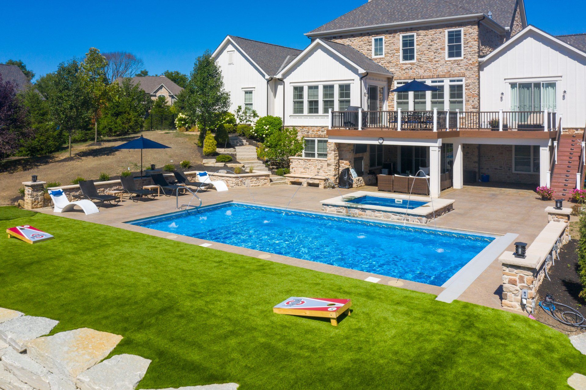 Backyard with a large blue swimming pool, patio seating, and a two-story house under a clear sky