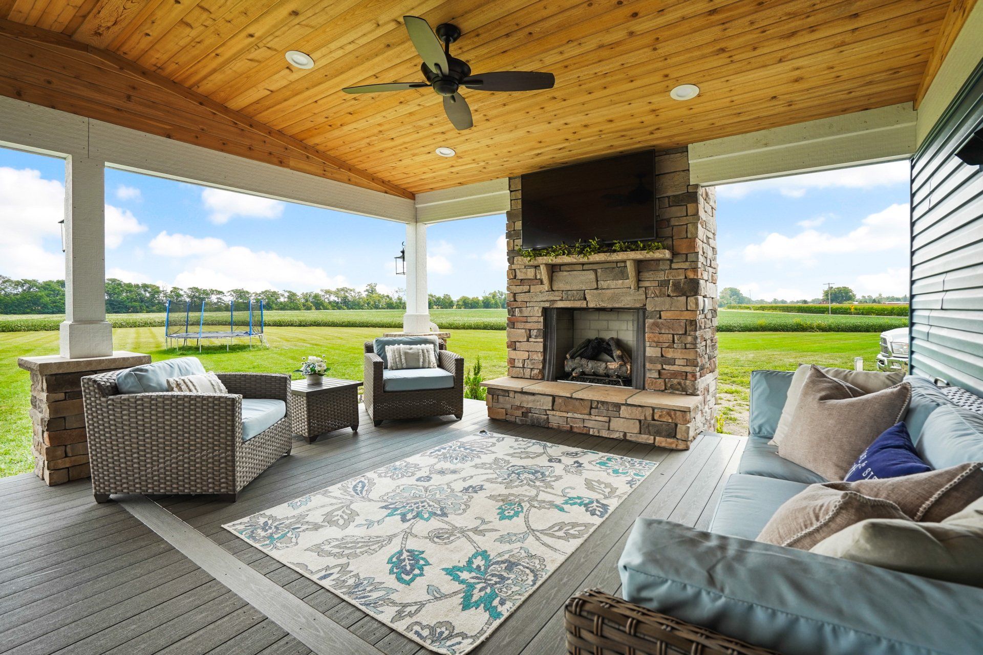 Covered patio with stone fireplace, wicker seating, and views of green fields and water