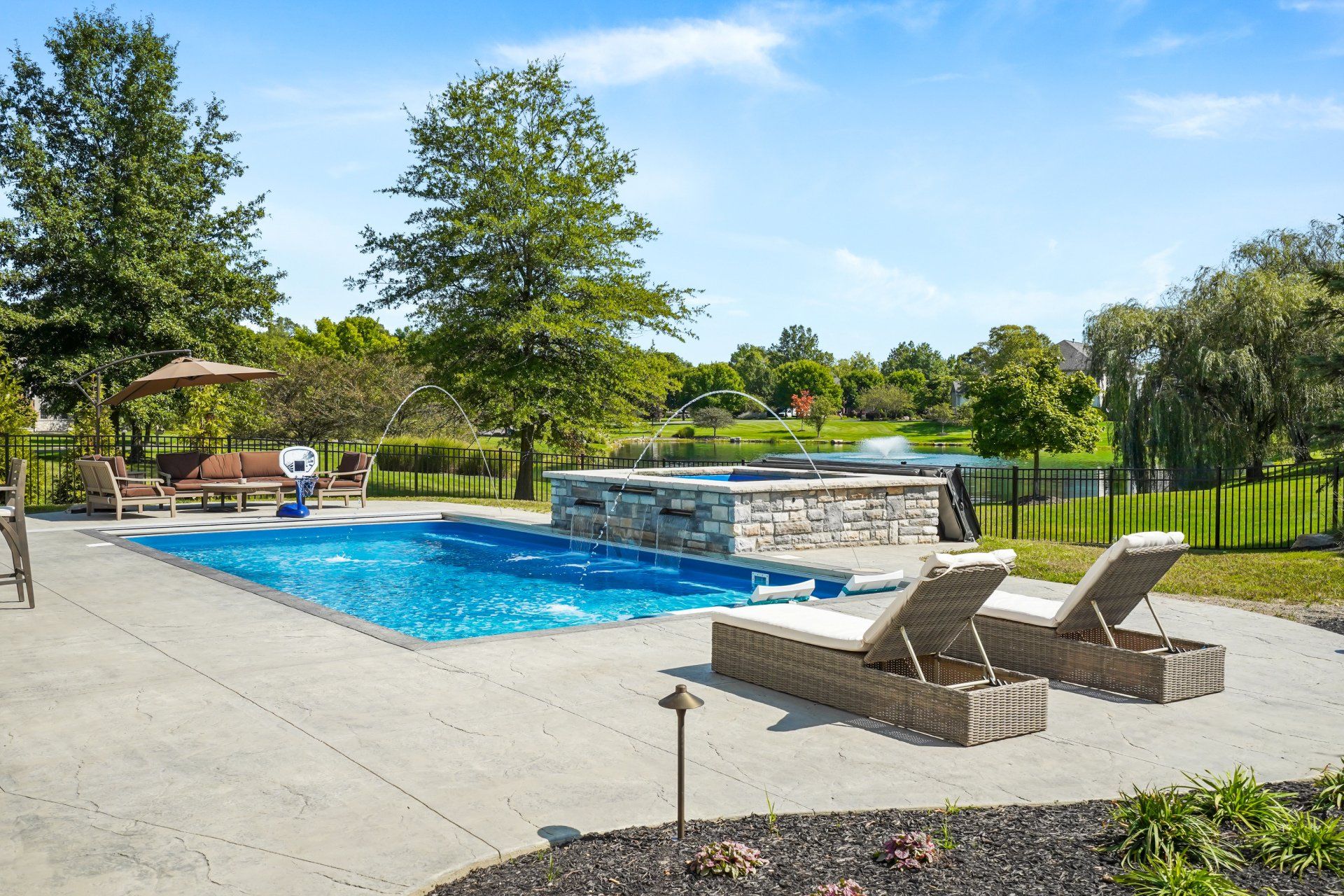 Outdoor pool with blue water, stone waterfall, and white lounge chairs on a sunny patio surrounded by trees