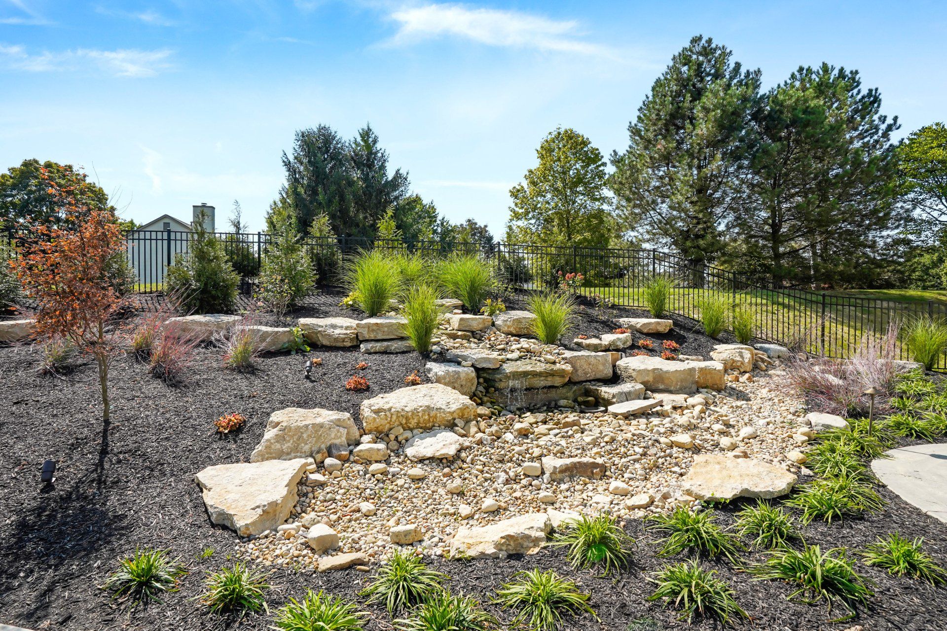 Landscaped garden with stone path, gravel beds, and trees under a clear blue sky
