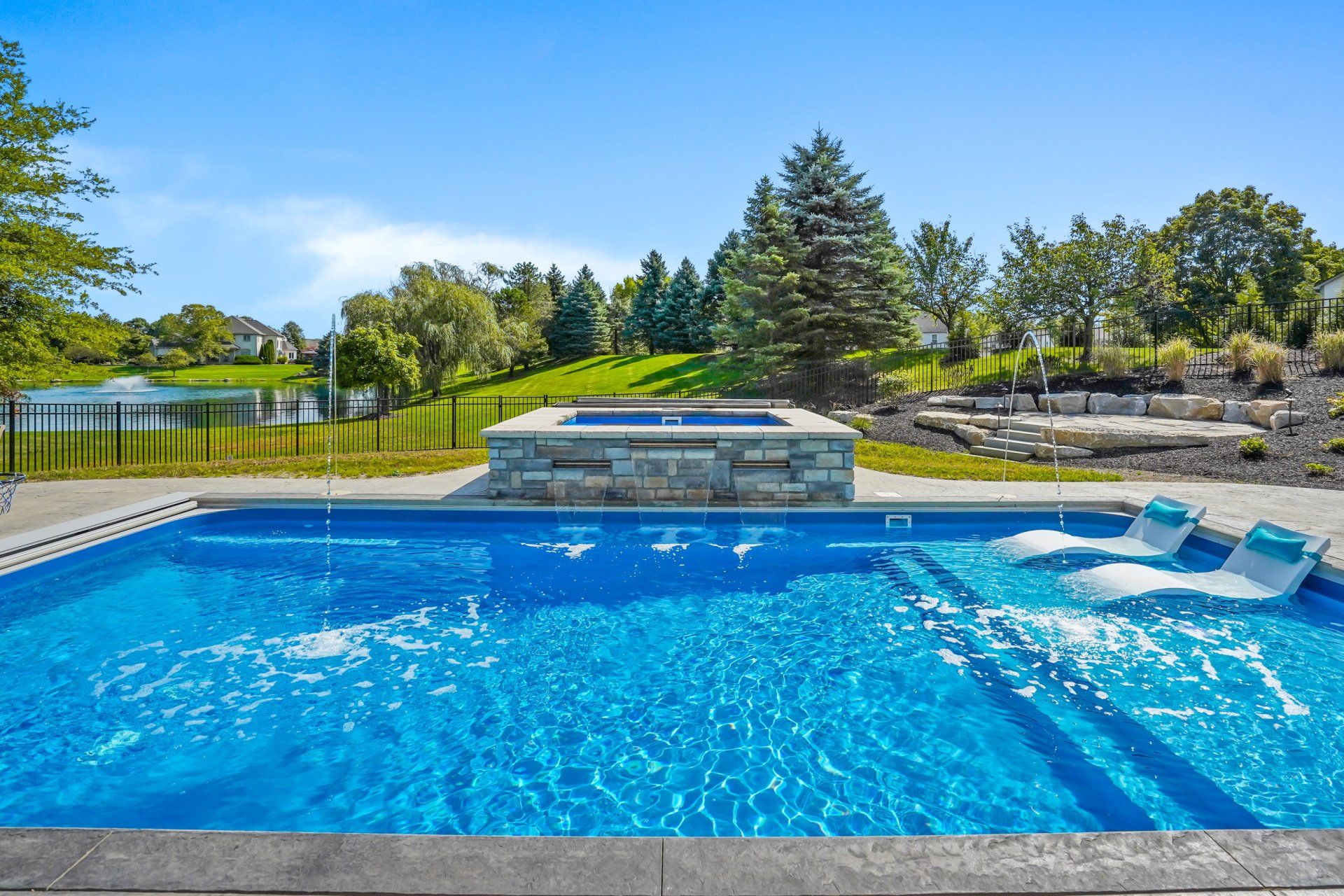 Blue backyard swimming pool with lounge chairs and a landscaped patio on a sunny day