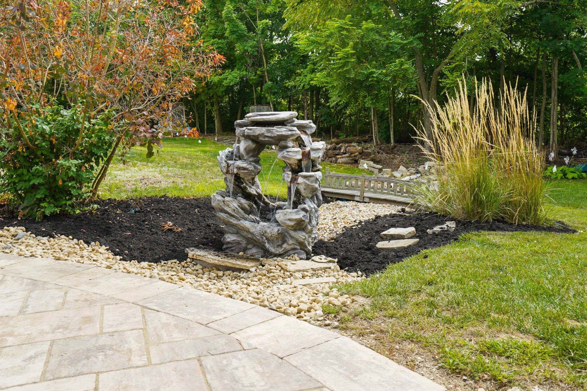 Garden stone sculpture beside a curved patio, surrounded by mulch, grass, and trees