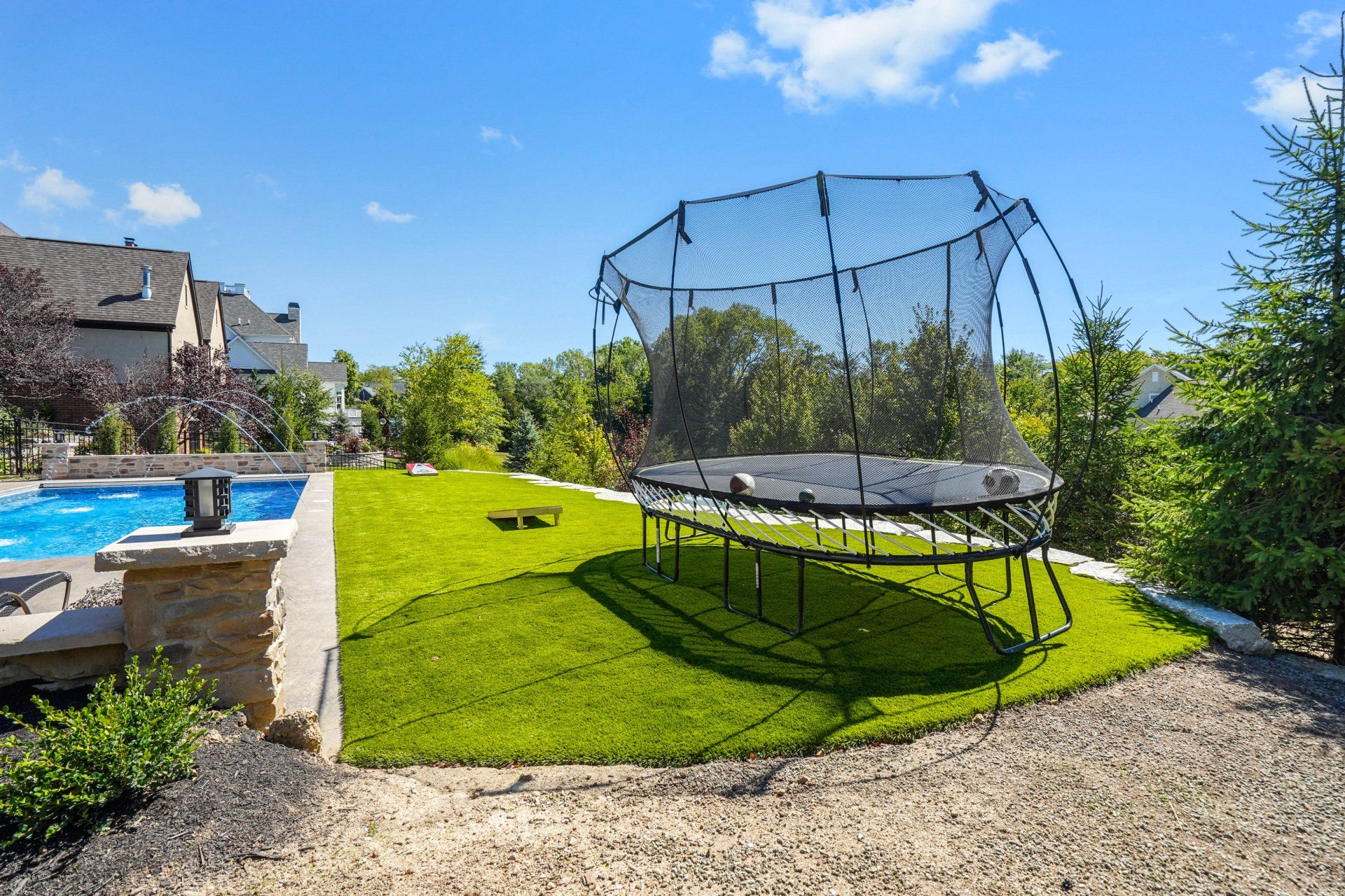 Backyard with trampoline on green lawn beside a swimming pool and gravel path