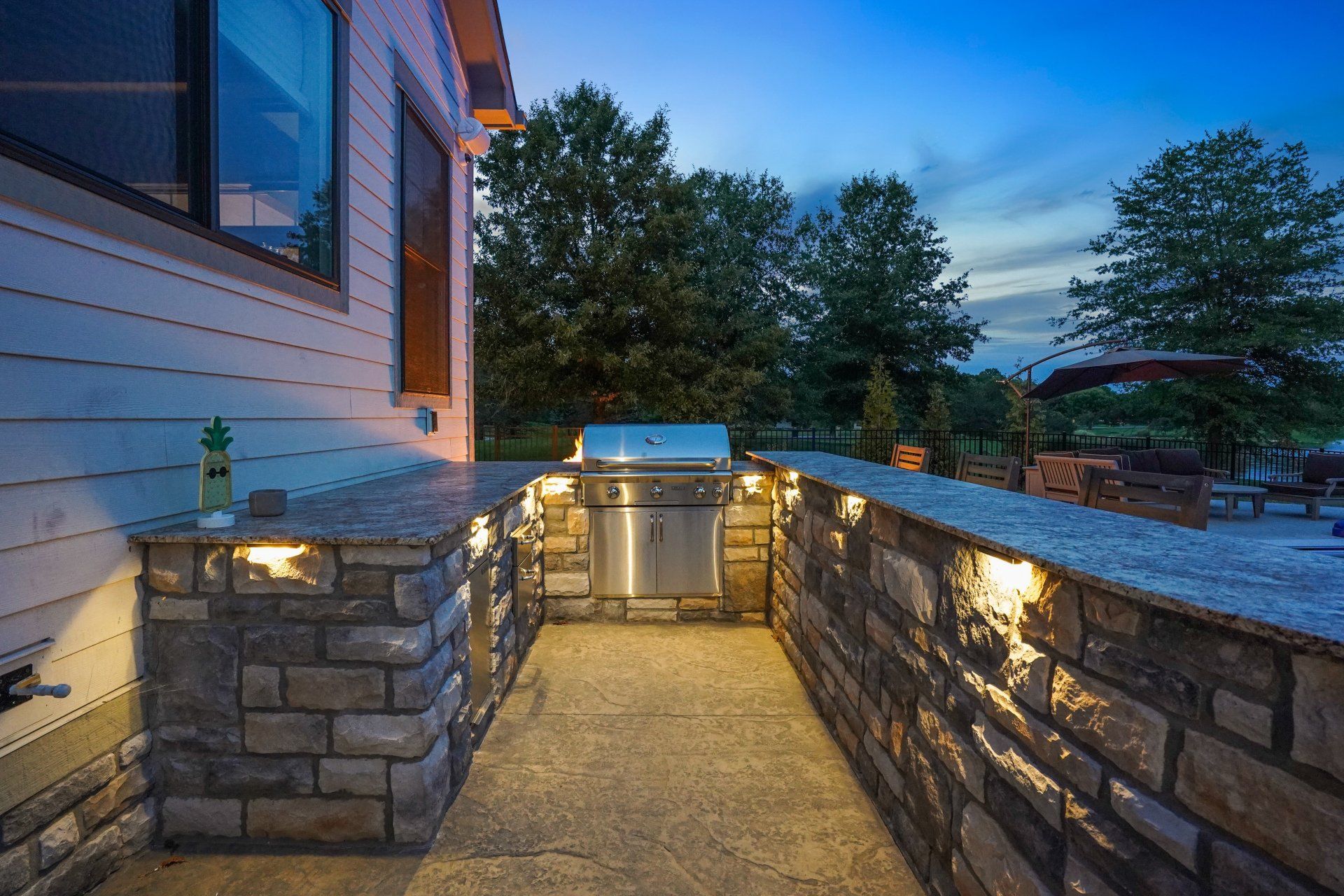 Stone patio walkway beside a house at dusk, lined with warm lights and a gate at the end.