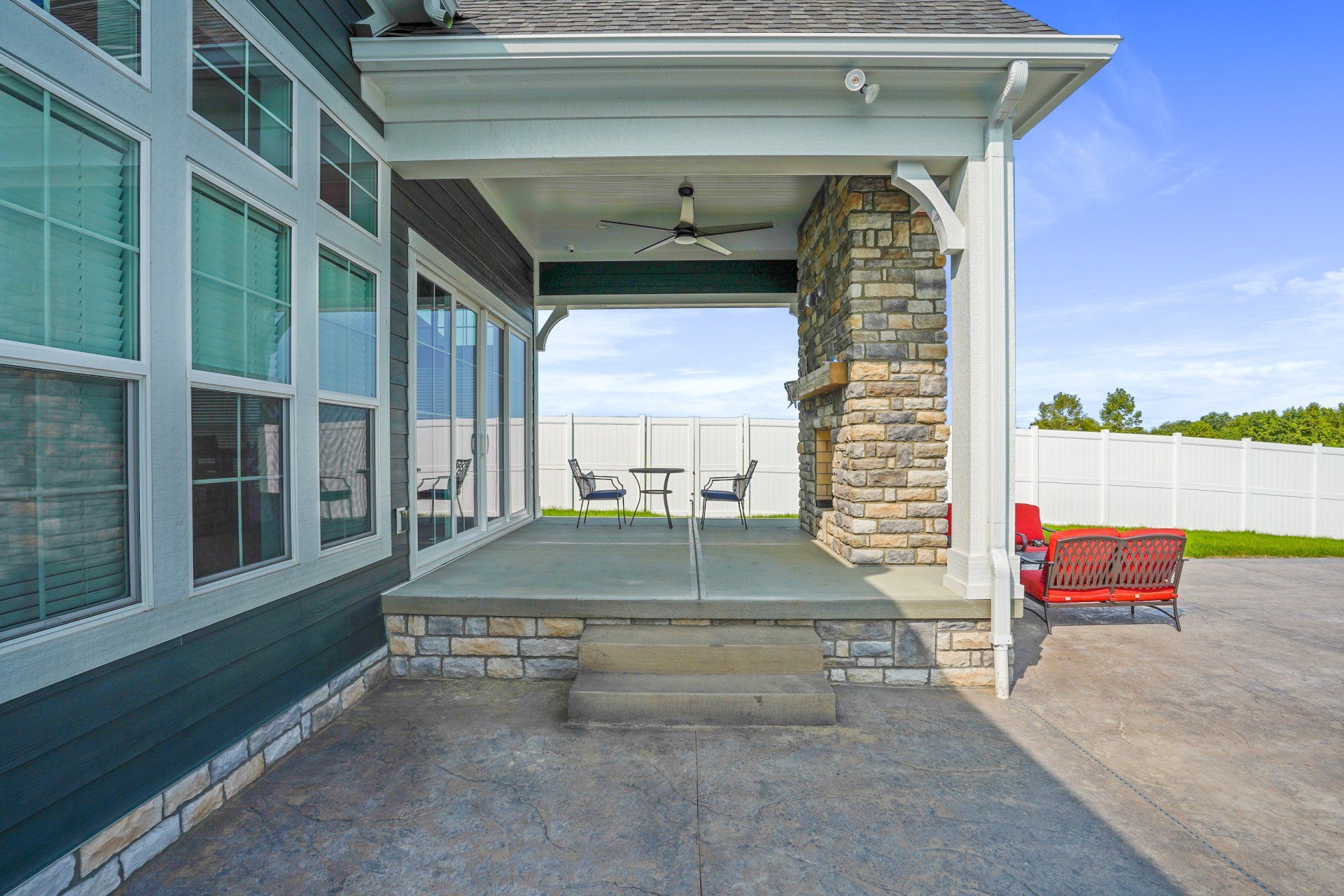 Covered concrete porch with stone column, windows, and a red bench beside a driveway.