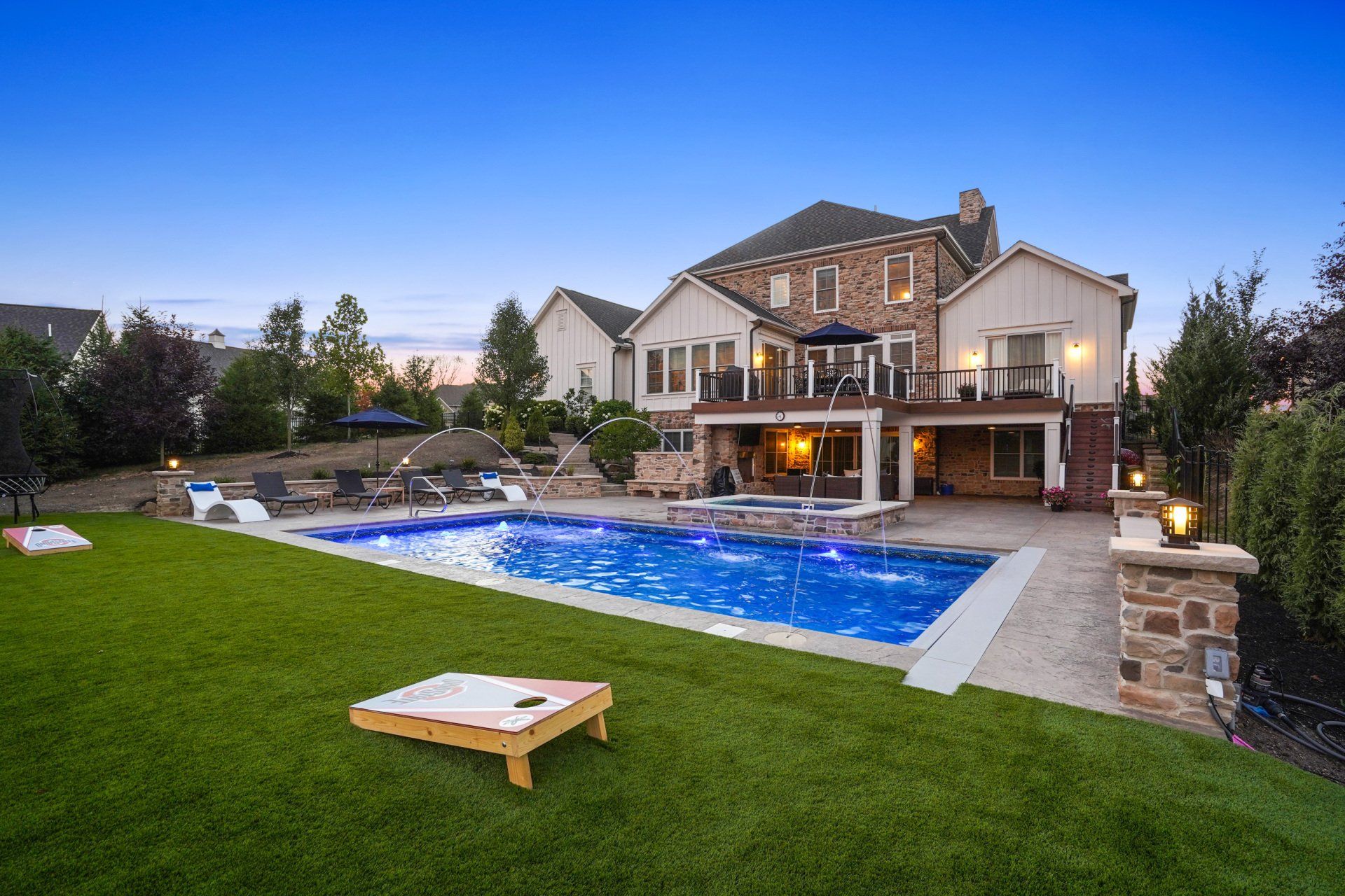 Luxury house with a lit backyard pool, patio, and manicured lawn at dusk