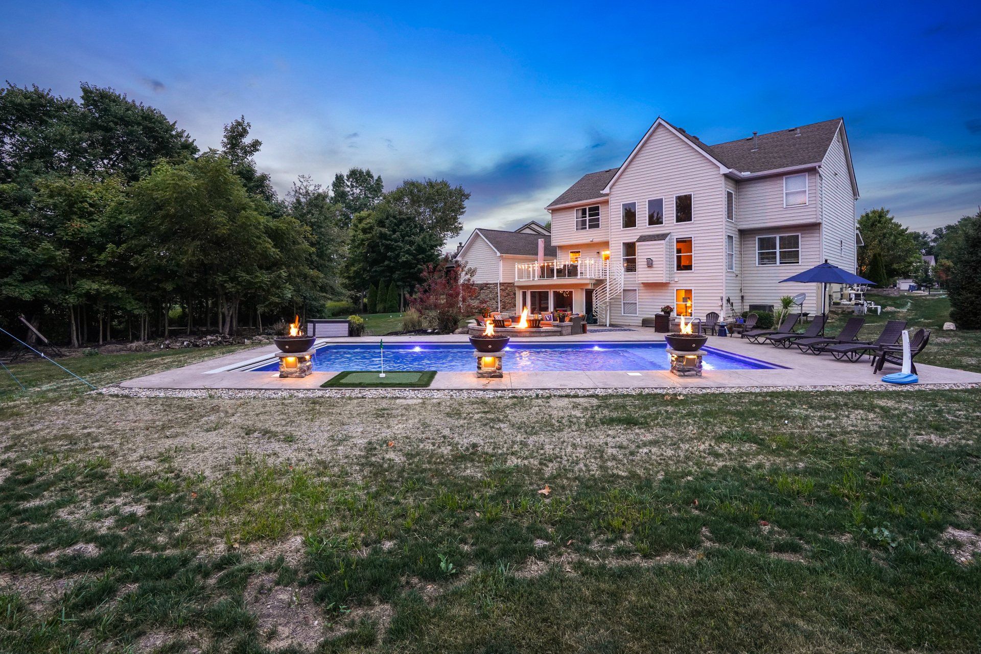 Luxury house with lit backyard pool and fire features at dusk